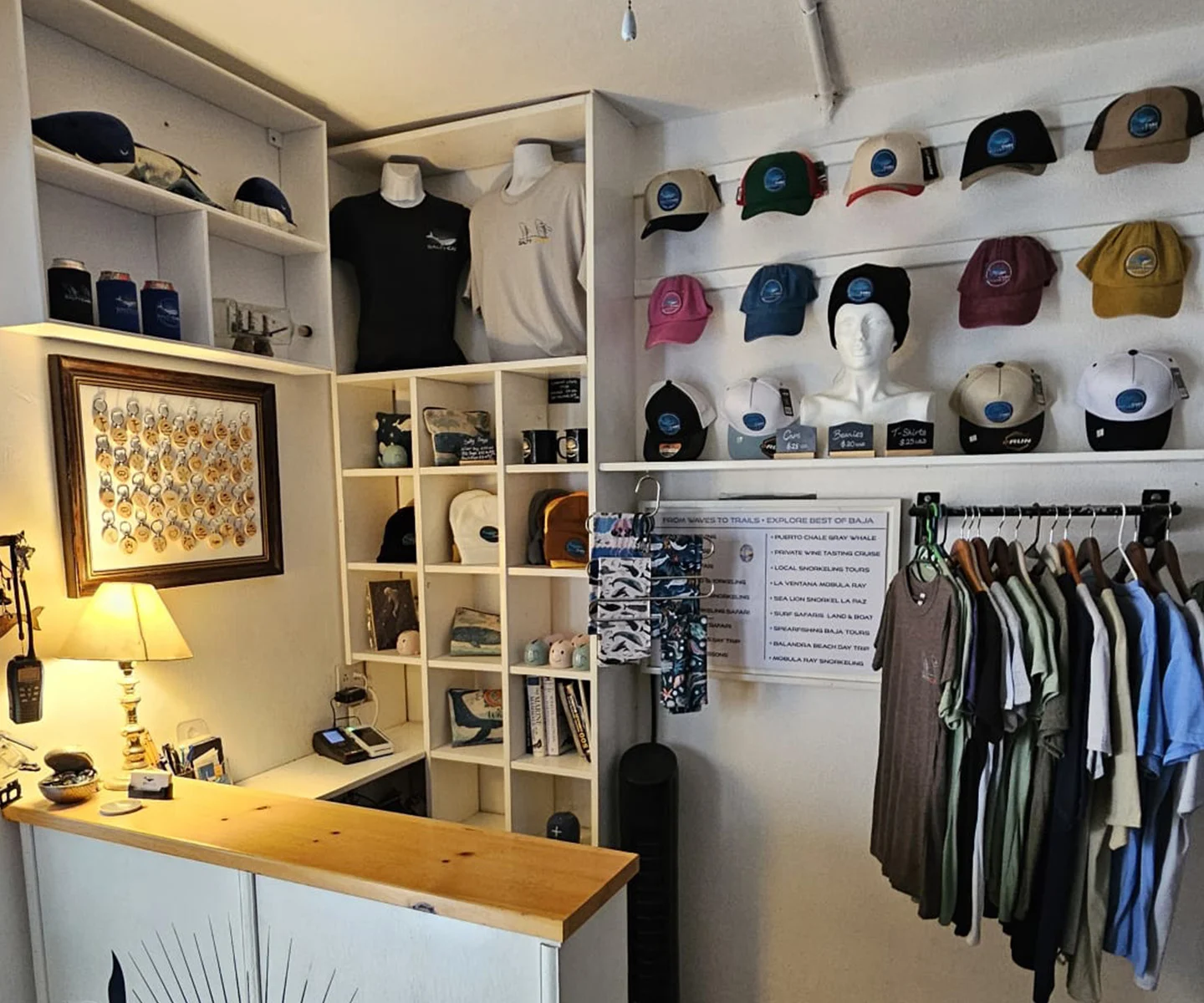 Interior of the Salty Cabo Excursions office at Marina Puerto Los Cabos, featuring the reception desk, souvenir hats, T-shirts, and gifts for visitors.