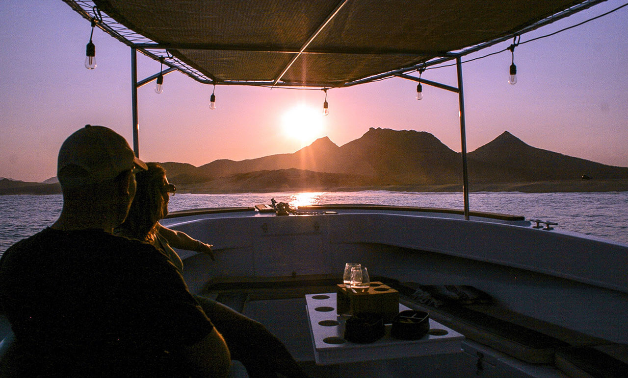 Couple enjoying a sunset cruise aboard Salty Cabo’s boat, overlooking the Sea of Cortez and El Picacho mountain in San José del Cabo.