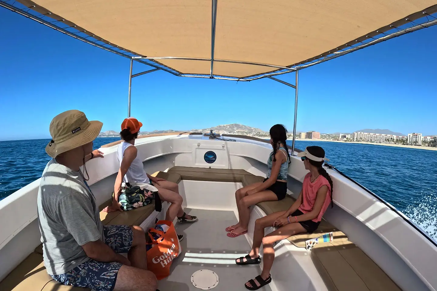 Guests relaxing under the shaded canopy aboard the Super Salty tour boat while cruising along the San José del Cabo coastline in the Sea of Cortez.